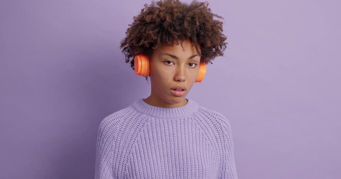 Rude impolite woman looks dissatisfied at someone shows middle finger expresses her disrespect and disagreement has resentful look then crosses arms wears headphones isolated over purple wall