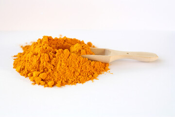 A pile of dry turmeric, and a wooden scoop for spices on a white background. Selective focus. Empty space for text or inscription.