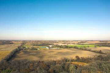 Fototapeta premium Beautiful aerial of farm fields in rural Wisconsin in autumn with patches of bare trees, barns and silos spread across the landscape beyond.