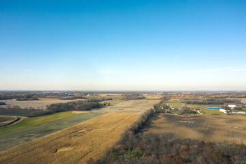 Beautiful aerial of farm fields in rural Wisconsin in autumn with patches of bare trees, barns and silos spread across the landscape beyond.