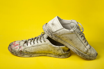 Dirty shoes, vintage white torn sneakers isolated on a yellow background.