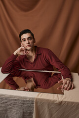 Fototapeta premium Handsome guy in a shirt posing at a table indoors on a fabric background and a square mirror