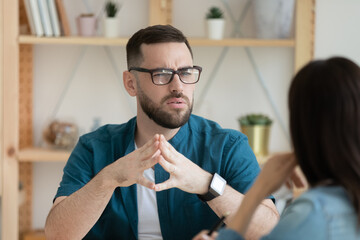 Unhappy young Caucasian man worker talk with female colleague thinking doubting at office meeting....