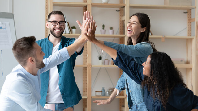 Wide banner panoramic view of overjoyed multiracial employees give high five celebrate shared team business success in office. Smiling colleagues have fun engaged in teambuilding activity at meeting.