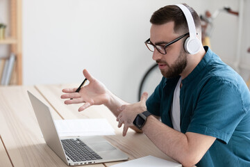 Focused Caucasian businessman in headphones look at laptop screen have video call with client online. Serious male employee in earphones have webcam digital virtual conference on computer in office.