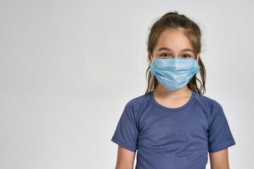 Portrait of little sportive girl child in sportswear wearing medical mask while standing isolated over white background
