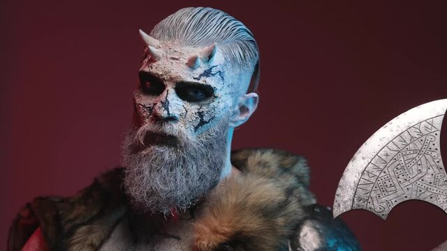 Frosty barbaric undead with horns and white skin with beard posing in dark red background with his huge double axe looking at camera with blue eyes and rotating his head.