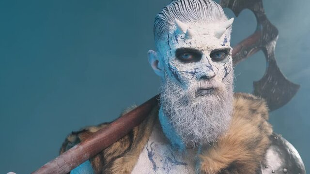 Mystic and dangerous king of the dead with pale skin in light armour with fur posing in dark blue background looking around and holding his double axe on his shoulder.