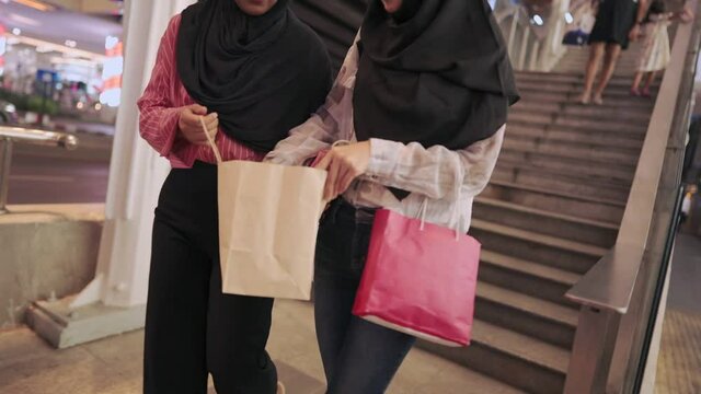 Two asian muslim females on weekend shopping nights, walking down from the stairs, consumer credit card member points redemption, duty free products, urban city life walking along the street side