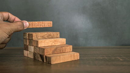 Close-up hand is placing wood block tower stacked in pyramid shape with caution to prevent collapse...