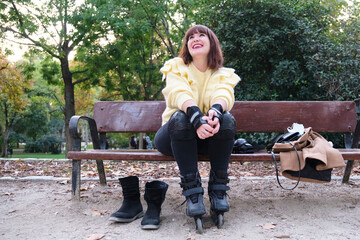 Young caucasian woman sitting in a bench with her roller skates on looking at the sky. Outdoor...