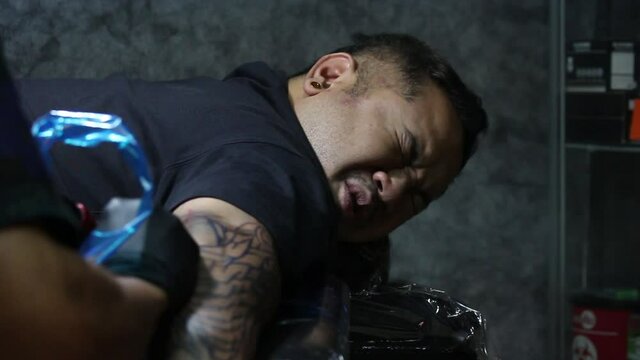 Close up shot of man face feeling pained from Tattooist making tattoo on his arm. facial expression of suffering