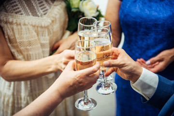 Guests and relatives of different ages at the wedding raise their glasses with festive champagne. Hands with drinks close-up. Marriage celebration, congratulations.