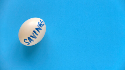 Savings concept. Top view of an egg written with SAVINGS on a blue background with copy space.