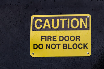 View of yellow sign Caution Fire Door Do Not Block against the black background