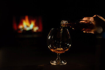 Close-up of a female hand with a glass of brandy on the background of the fireplace