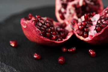 broken into pieces pomegranate fruit on a black round stand of slate black background