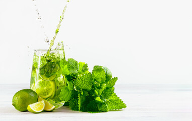 Mojito pours into a glass with splash on a light background, two jets, with limes, a bunch of mint and ice. One of set mojito.
