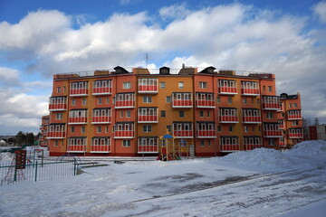A residential brick apartment building with a playground in front of it stands among the snow in the village of Taezhny, Krasnoyarsk Territory. Russia.