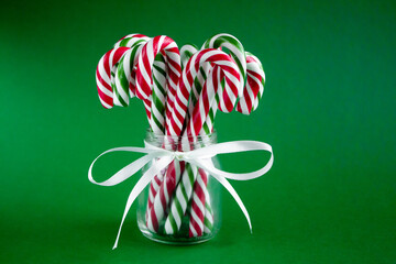 Christmas background with candy canes. Red and green sweet sticks with white ribbon in the glass jar. Poster, banner, greeting card template. Festive backdrop. Holiday season