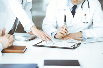 Group of unknown doctors are sitting at the desk and discussing medical treatment, using a clipboard, close-up. Team of physicians at work in a clinic. Medicine and healthcare concept