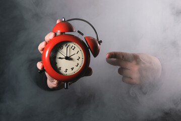 Red alarm clock in female hand close up on the dark smoky background.