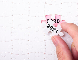 Hand putting a piece of 2021 white jigsaw puzzle and close up a year 2020.