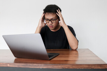 Young Asian man feeling stress and confuse with work in laptop. Indonesia Man wear black shirt Isolated grey background.