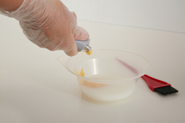 Woman preparing dye for hair coloring at white table, closeup