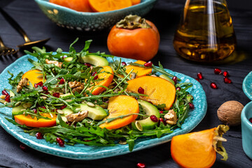 Fresh fruit salad with persimmons, arugula, avocado, pumpkin seeds, walnuts, pomegranate on a wooden background, Diet menu. Vegan food. Food recipe background. Close up