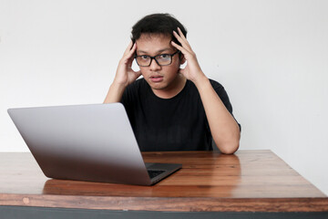 Young Asian man feeling stress and confuse with work in laptop. Indonesia Man wear black shirt Isolated grey background.