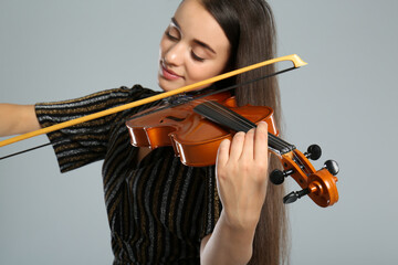 Beautiful woman playing violin on grey background, focus on hand