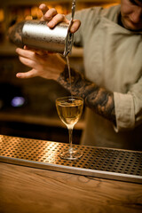 barman carefully pouring drink from measuring cup into glass at the bar