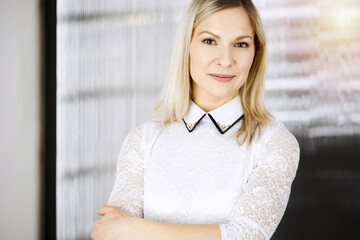 Friendly adult business woman standing straight. Business headshot or portrait in sunny office