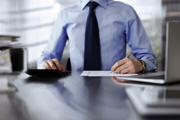 Unknown man accountant in blue shirt use calculator and computer with holding pen on while staying at home during covid pandemic. Taxes and audit concept