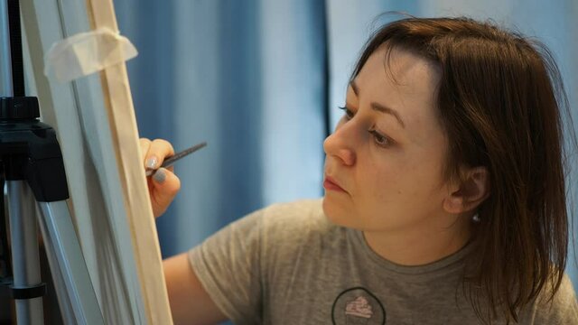 a young woman draws a picture with a brush on an easel in the room.