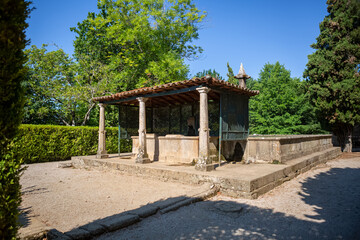 View of old structure with granite pillars and orange ceramic tile roof, with fountain in the interior and exterior tank, inserted in the Gardens of Solar de Mateus