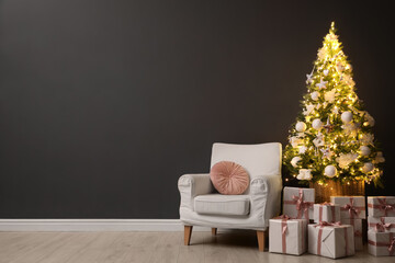 Beautifully decorated Christmas tree, gift boxes and armchair near black wall indoors, space for text