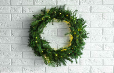 Beautiful Christmas wreath with festive lights on white brick wall