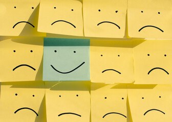 positive attitude or the concept of optimism - a happy smiley face on a yellow sticky note surrounded by sad unhappy blue faces