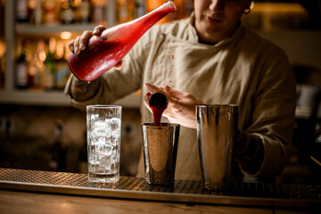 bartender holds bottle in hand and with other hand pours juice from jigger into shaker