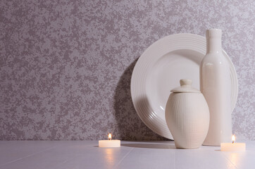 Relaxation nordic home decor in evening with glowing candles, white simple ceramic crockery in moonlight on white table, copy space.