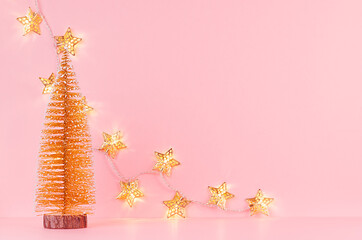 Christmas background in gold glitter color - christmas tree and glowing star lights on light pink background, copy space.