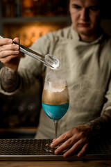 man holds piece of ice over wine glass decorated with gold