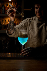 guy at dark bar holds golden piece of ice over steaming wine glass