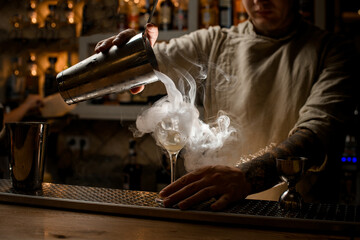 view of bartender pouring steaming drink from shaker cup into wine glass