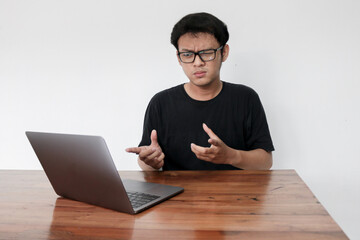 Young Asian Man is confused and shocked when calling in the phone with the laptop beside it. Indonesian man wearing a blue shirt