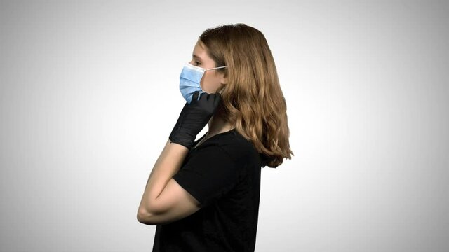 Woman showing how to use a surgical mask,  signing "thumbs up", wearing gloves, medium shot over white background.