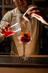 professional barman masterfully add ingredients to glass with vegetables inside and makes fire over it