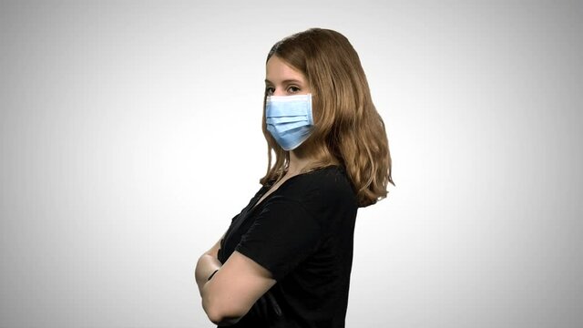 Woman with a surgical mask and gloves standing with cross arms and looking dramatically, over white background.